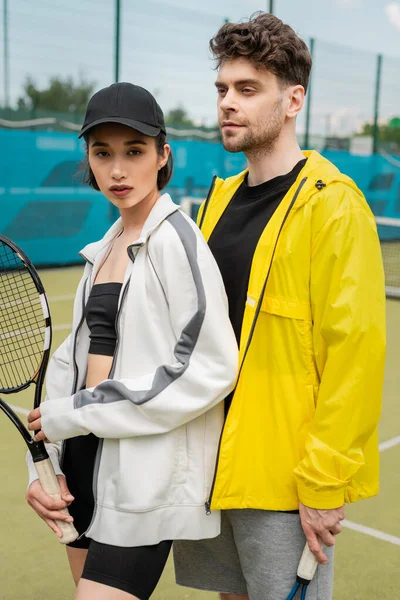 Deporte, hombre y mujer de moda de pie en la cancha con raqueta de tenis, pareja deportiva, pasatiempo - foto de stock
