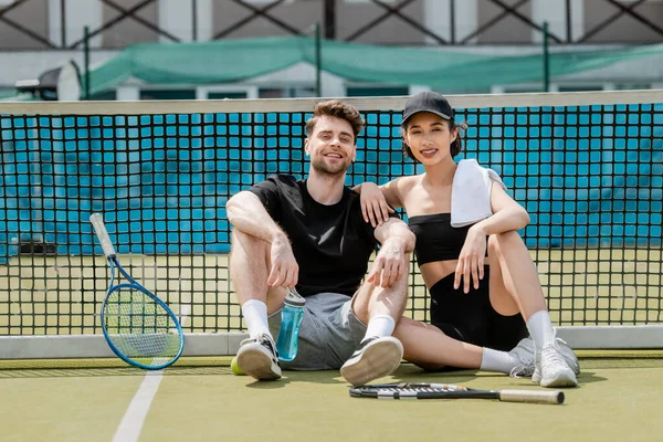 Здоровий спосіб життя, щасливий чоловік і жінка в активному вбранні відпочивають біля тенісної мережі на корті, ракетки — стокове фото