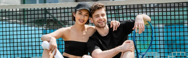 Banner, happy man and woman in sportswear resting near tennis net on court, looking at camera — Stock Photo