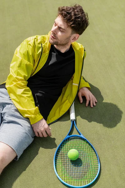 Coup de tête, bel homme se reposant près de la balle de tennis et de raquette, joueur de tennis masculin sur le court — Photo de stock