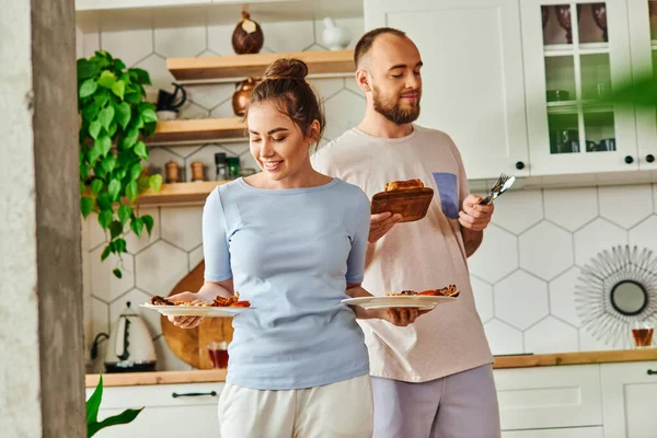 Позитивна жінка тримає сніданок біля хлопця з столовими приборами і хлібом вдома вранці — стокове фото