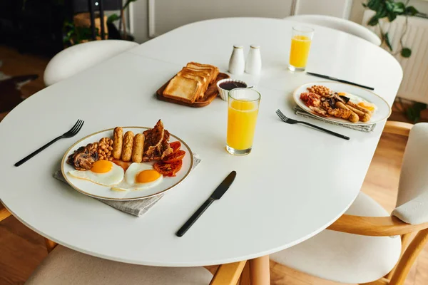 Pequeno-almoço saboroso com ovos fritos perto de torradas e suco de laranja na mesa em casa de manhã — Fotografia de Stock