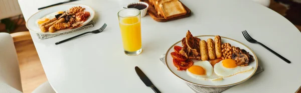 Delicioso desayuno con huevos fritos, salchichas y jugo de naranja en la mesa en casa, pancarta - foto de stock