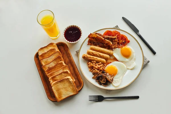 Вид зверху смачний сніданок зі смаженими яйцями, ковбасками та тостами біля апельсинового соку та варенням на столі — стокове фото