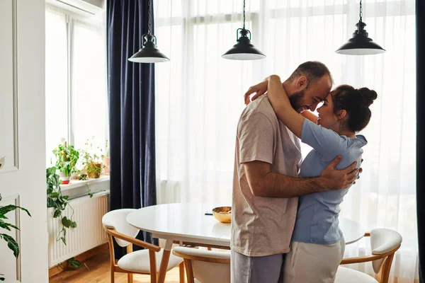 Vue latérale du couple souriant en tenue de maison s'embrassant et passant du temps à la maison — Photo de stock