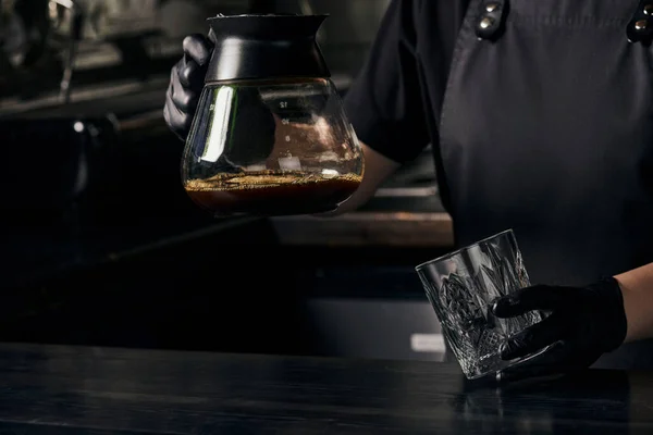 Barista in black gloves holding glass and coffee pot of freshly brewed aromatic espresso — Stock Photo