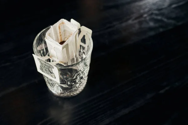 High angle view of crystal glass with ground coffee on black tabletop, pour-over brewing method — Stock Photo