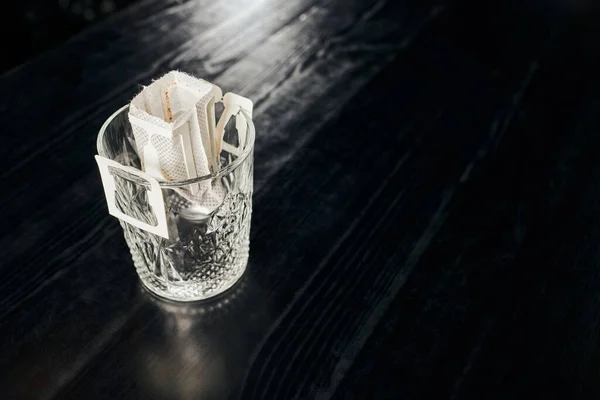 Glas mit frischem, aromatisch gemahlenem Kaffee in Filterbeutel auf schwarzer Holztischplatte, Übergießmethode — Stockfoto