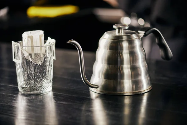 Glas mit gemahlenem Kaffee im Filterbeutel, metallischer Tropfkessel auf schwarzem Tisch, Aufgussverfahren — Stockfoto