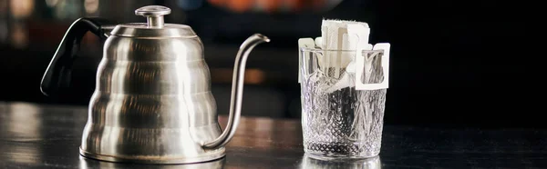 Espresso, Glas mit aromatischem Kaffee in Papiertüte neben Wasserkocher auf schwarzem Tisch, Banner — Stockfoto
