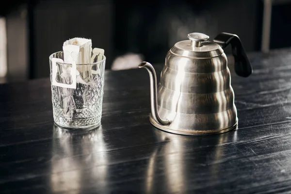 Pour-over method, glass with coffee in paper filter, metallic drip kettle on black wooden table — Stock Photo