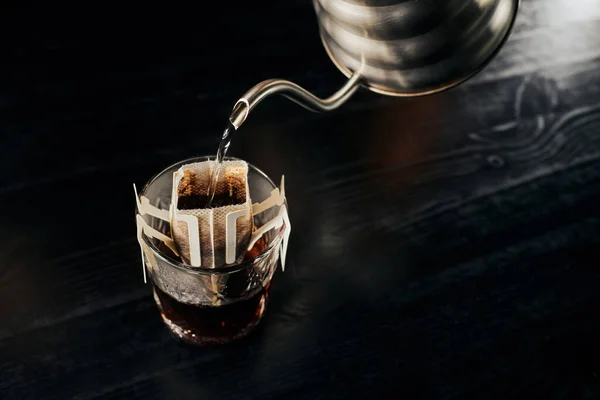 Залить-над эспрессо, наливая кипящую воду из капельного чайника в стекло с кофе в фильтр мешок — стоковое фото