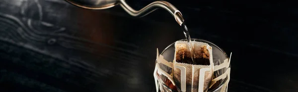 Boiling water pouring from metallic kettle into glass with ground coffee in paper filter bag, banner — Stock Photo