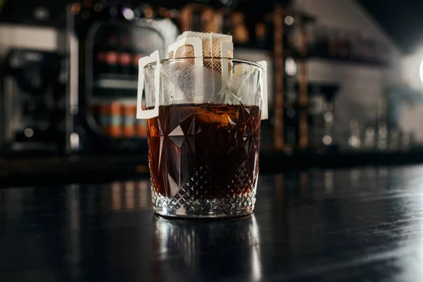 Método de gotejamento de café expresso, vidro de cristal com café em saco de arquivador de papel na mesa de madeira preta no café — Fotografia de Stock