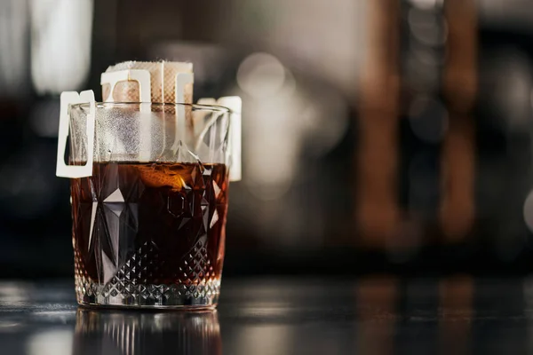 Хрустальное стекло, молотый кофе в бумажном мешке фильтра на черном деревянном столе в кафе, метод капельного эспрессо — стоковое фото