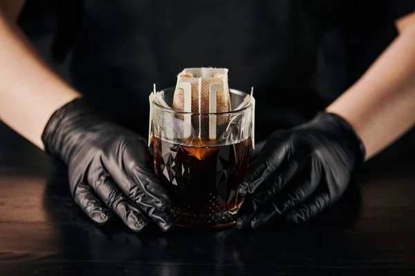 Barista in black latex gloves brewing espresso, glass with ground coffee in filter bag, drip method — Stock Photo