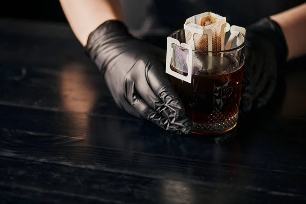 Pour-over método de fabricação de cerveja, vidro com café em saco de filtro de papel perto barista em luvas de látex preto — Fotografia de Stock