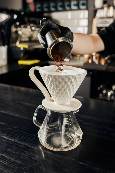Barista adding fine grind coffee from jigger into ceramic dripper on glass pot, V-60 style method — Stock Photo