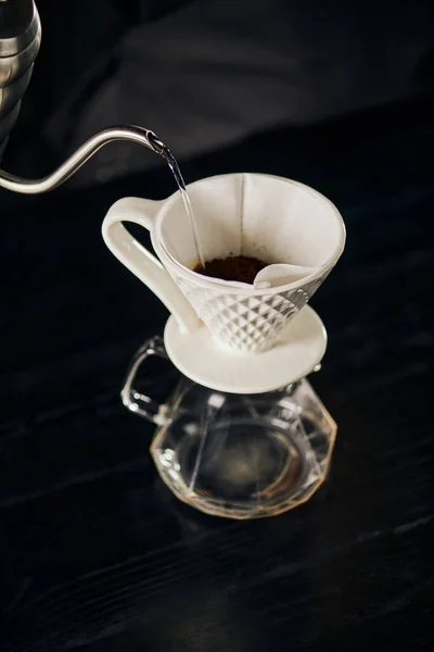 Acqua bollente versata su caffè macinato in gocciolatore di ceramica posto su pentola di vetro, espresso in stile V-60 — Foto stock