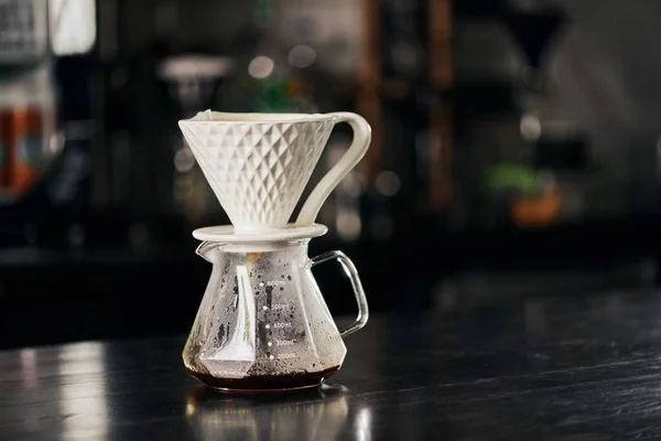 Método espresso estilo V-60, gotero de cerámica en maceta de vidrio con café recién vertido sobre mesa negra - foto de stock