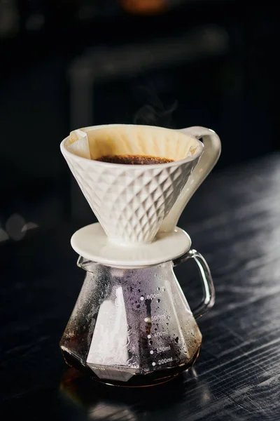 Ceramic dripper with pour-over coffee on glass pot in cafe on black table, alternative V-60 style — Stock Photo