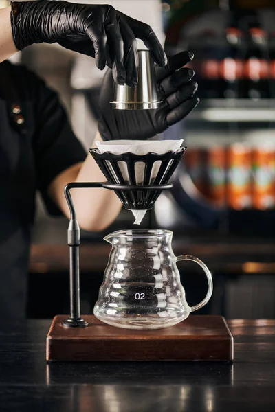 Barista segurando jigger acima do suporte gotejador com filtro de papel e panela de café de vidro, V-60 estilo espresso — Fotografia de Stock