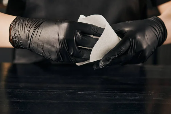 Частичный вид баристы в черных латексных перчатках с бумажным мешком фильтра для кофе над черным столом — стоковое фото