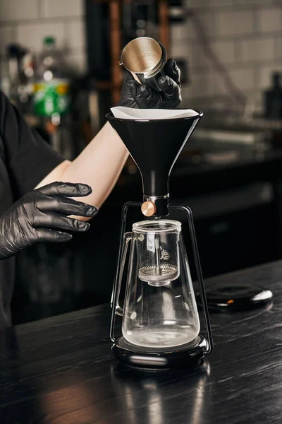 Ausgeschnittene Ansicht des Barista in schwarzen Handschuhen, der Jigger in der Nähe der zusammengebauten Siphon-Kaffeemaschine im Café hält — Stockfoto