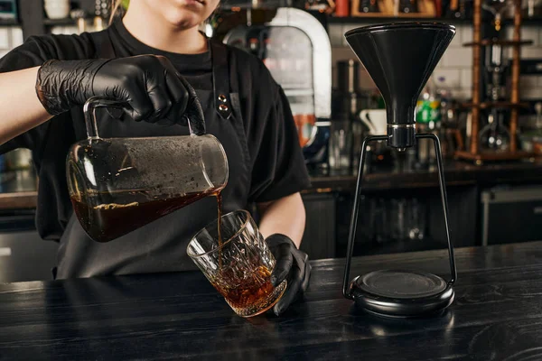 Partial view of barista pouring fresh espresso into crystal glass near siphon coffee maker in cafe — Stock Photo