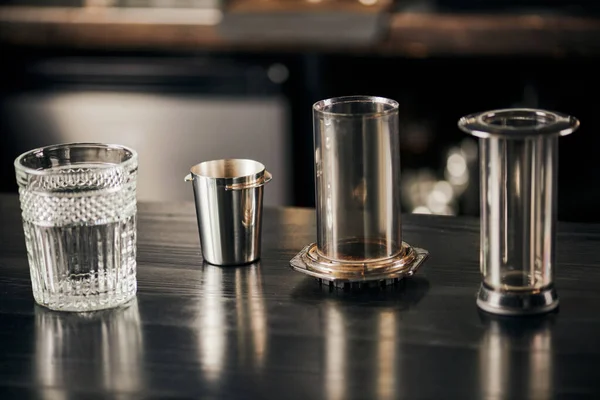 Vidro de cristal e partes de aero imprensa cafeteira na mesa de madeira preta no café moderno — Fotografia de Stock