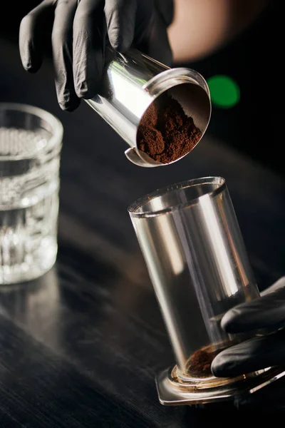 Barista in black latex gloves pouring ground coffee in aero press, alternative brewing method — Stock Photo