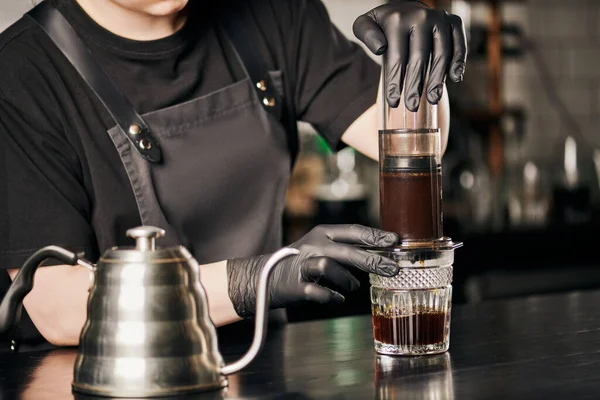 Vista parcial do barista em luvas pretas e avental preparando café expresso em aero imprensa perto de chaleira gotejamento — Fotografia de Stock
