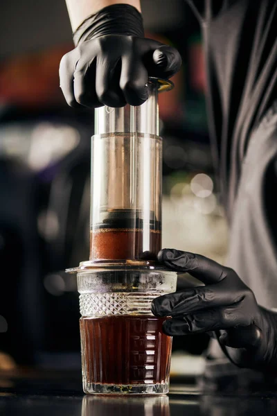 Barista in black latex gloves pressing ground coffee in aero press, alternative brewing method — Stock Photo