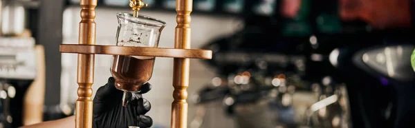 Partial view of barista in black glove holding cold drip coffee maker with ground coffee, banner — Stock Photo