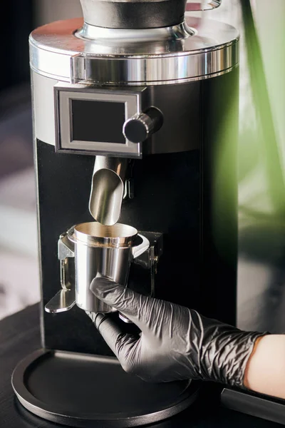 Vue recadrée du barista en gant de latex noir tenant la tasse à mesurer près du moulin à café électrique — Photo de stock