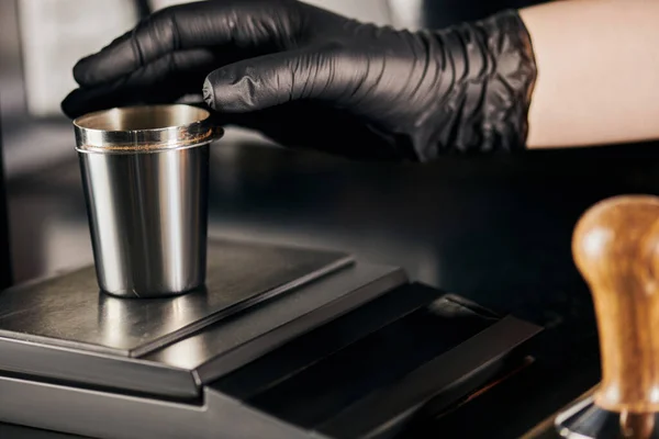 Vista parcial, barista profissional em luva de látex preto tendo copo de medição metálica no café — Fotografia de Stock