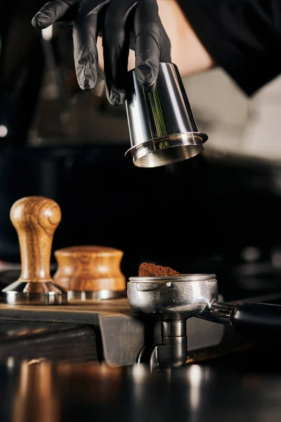 Vista cortada de barista em luva de látex preto segurando copo de medição perto portafilter — Fotografia de Stock