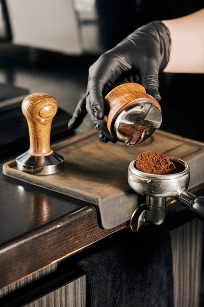 Cropped view of barista holding tamper and portafilter with aromatic coffee in coffee shop — Stock Photo