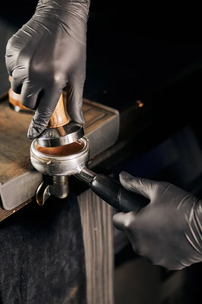 Обрізаний вид бариста в чорних латексних рукавичках, що пресують мелену каву в портативному фільтрі — стокове фото