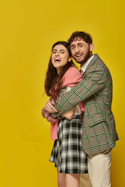 Щасливий чоловік обіймає молоду жінку сміючись, позує, жовтий фон, студентське вбрання, позитивність, стиль — стокове фото