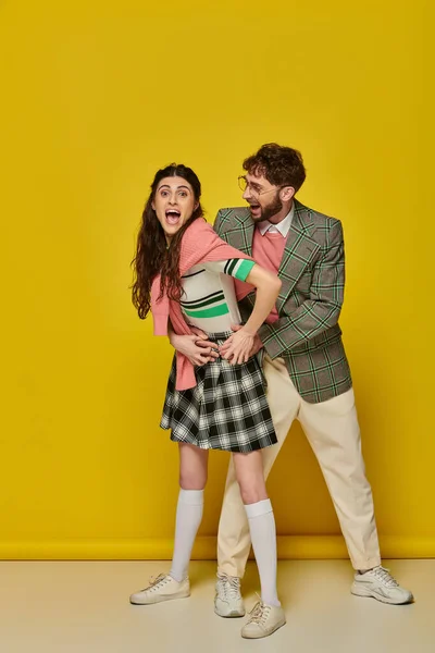 Alegre pareja divirtiéndose, hombre en gafas y mujer joven con la boca abierta, excitado, trajes de estudiante - foto de stock