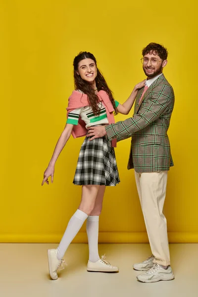 Freudiges Paar, das Spaß hat, Mann mit Brille umarmt junge Frau auf gelbem Hintergrund, Studenten, Outfits — Stockfoto
