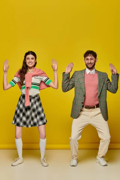 Coppia divertente, felice giovane uomo e donna gesticolare, in piedi su sfondo giallo, guardando la macchina fotografica — Foto stock