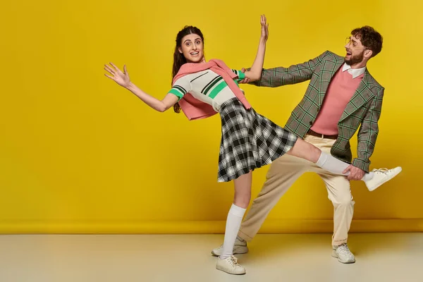Cheerful man in glasses catching falling woman, young couple, funny, yellow backdrop, emotional — Stock Photo