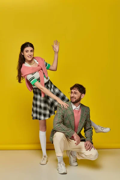 Couple drôle, jeune homme et femme heureux geste, posant sur fond jaune, tenue étudiante — Photo de stock