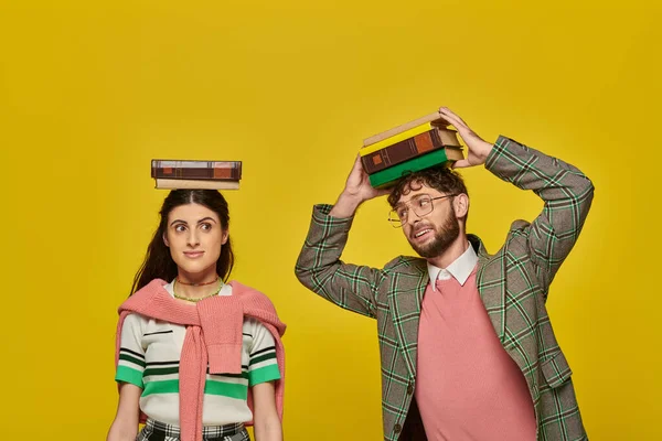 Ein paar Studenten, ein glücklicher junger Mann und eine junge Frau, die mit Büchern auf dem Kopf vor gelbem Hintergrund stehen, — Stockfoto