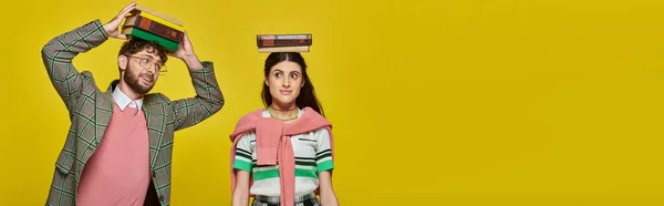 Couple of students, happy young man and woman standing with books on heads, yellow backdrop, banner — Stock Photo
