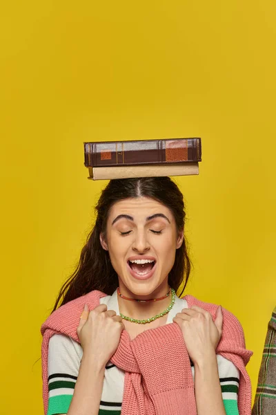 Excited woman with closed eyes standing with book on head, yellow backdrop, student life, young — Stock Photo