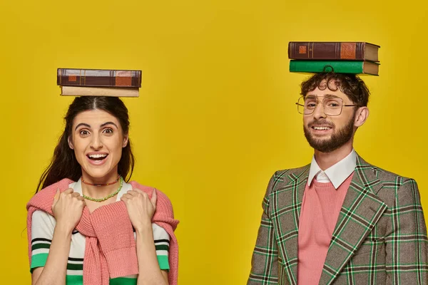 Pareja de estudiantes, hombre feliz y mujer emocionada de pie con libros sobre cabezas, fondo amarillo, joven - foto de stock