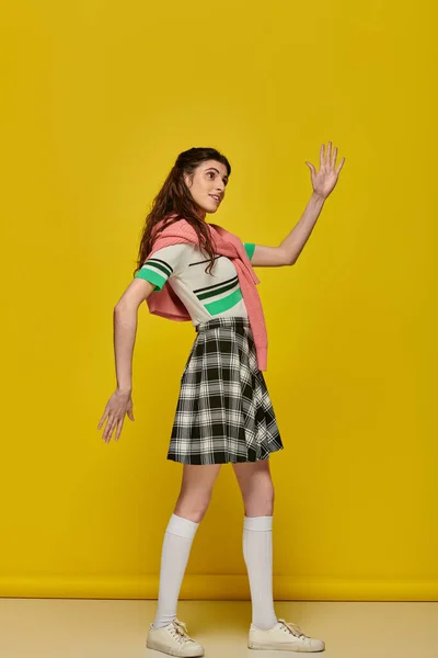 Young woman acting like a doll, gesturing unnaturally, standing on yellow backdrop, student — Stock Photo